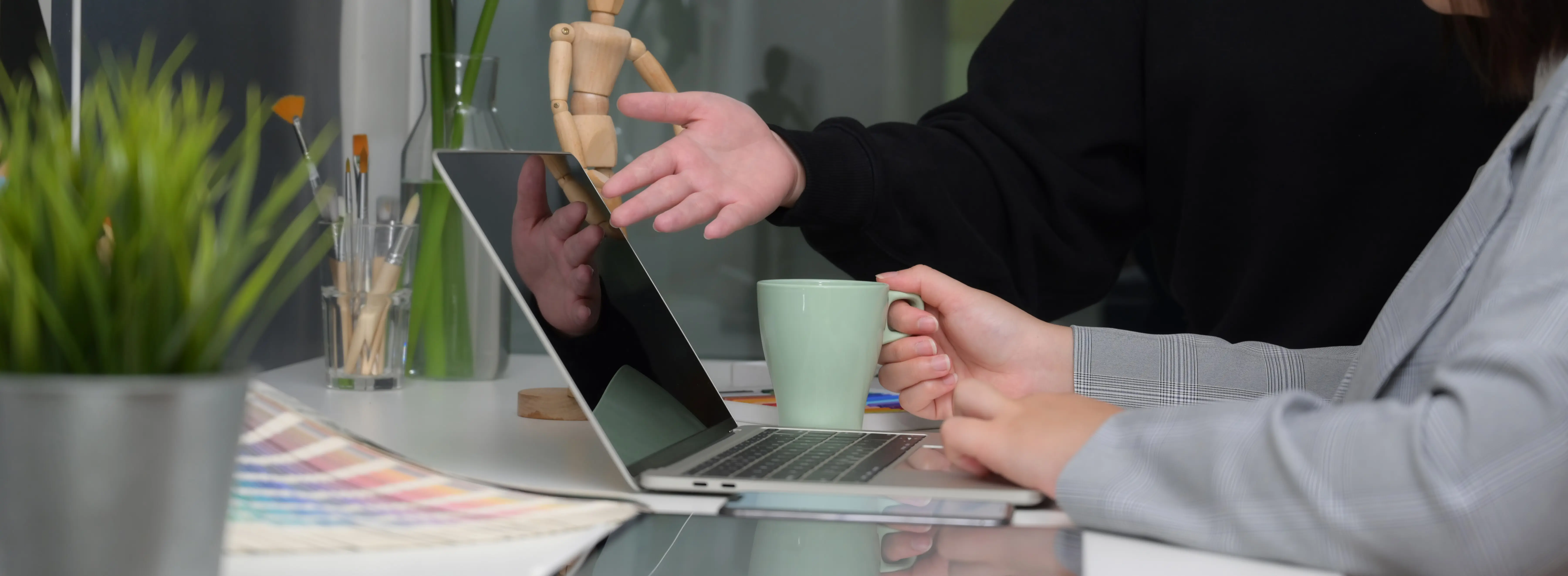 Seitenansicht von zwei Designern, die in einem durch Glas abgetrennten Büroraum ihr Projekt besprechen.