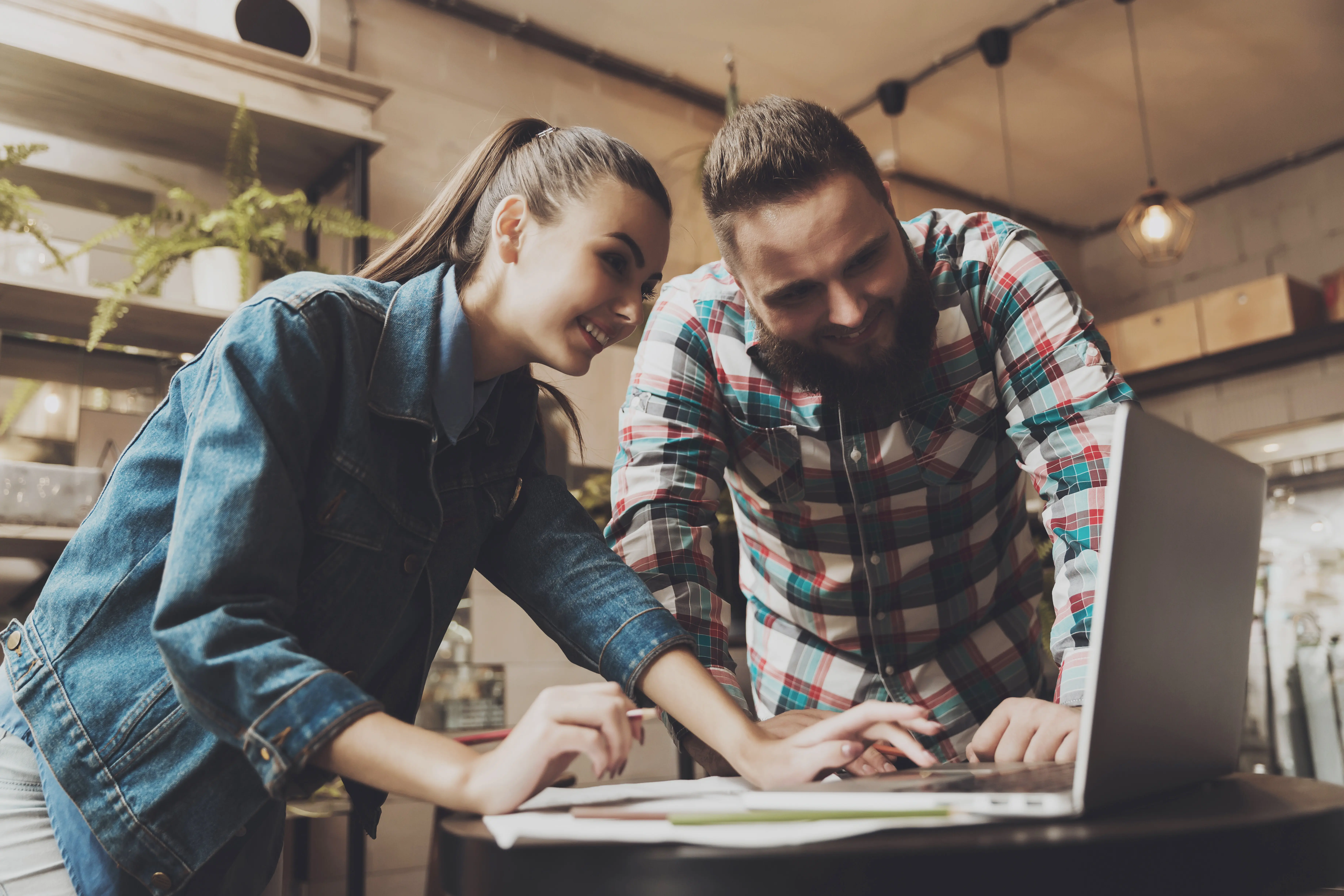 Zwei junge Menschen arbeiten in einem Café an einem Laptop.